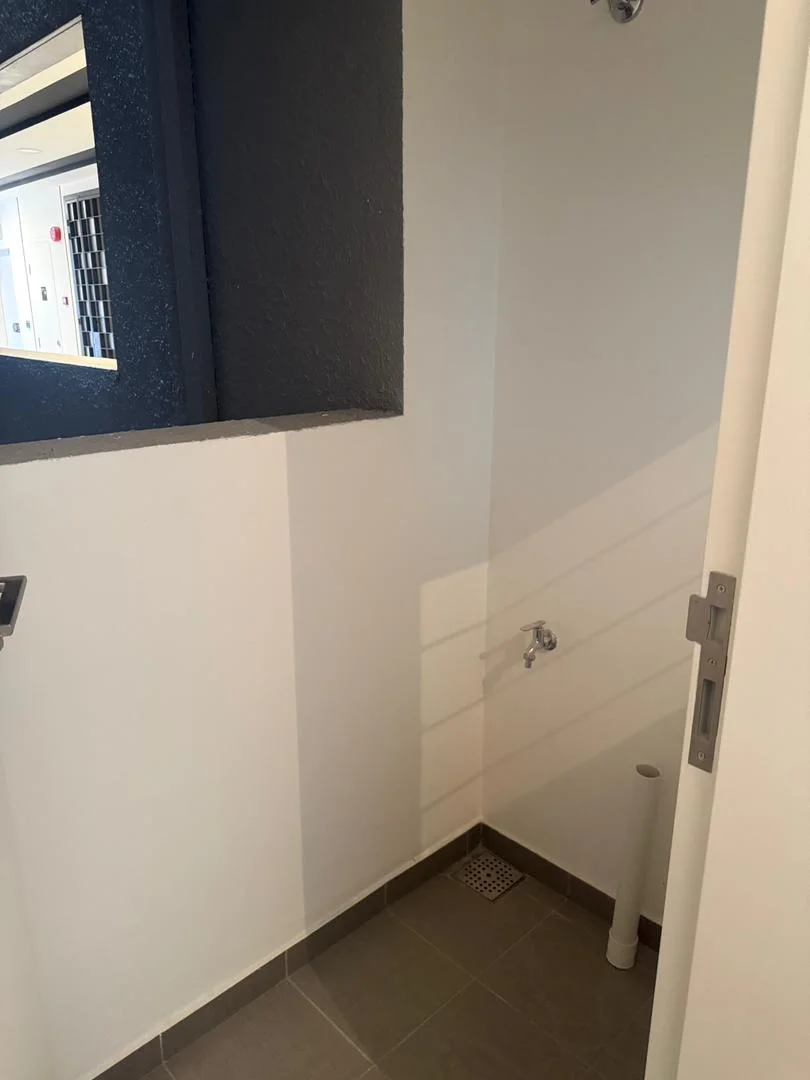 Room features: white painted walls, grey accent wall, tile flooring, shower head, drain in floor, wall-mounted faucet.