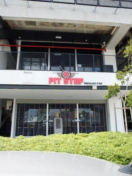 Exterior type: shophouse; features: glass facade, red signage with 'PIT STOP', metal grilles, outdoor seating area, manicured shrubs, two-storey structure, balcony on upper level, overhang roof; style: modern.