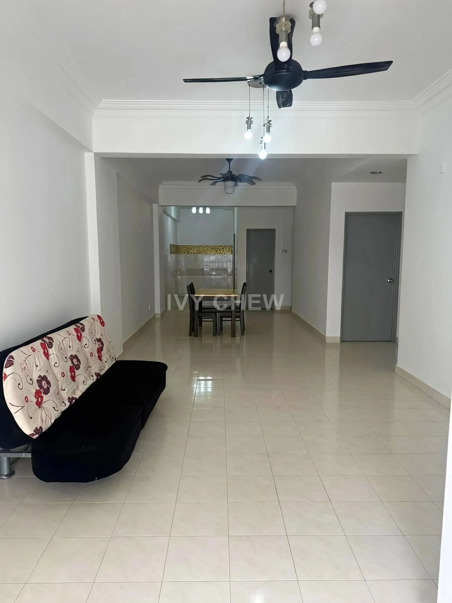 Living features: black fabric sofa with floral pattern, ceiling fan with light, white painted walls, cream tiled flooring, dining table with chairs visible in background, recessed ceiling lights, open layout to kitchen, natural light from windows; style: modern.