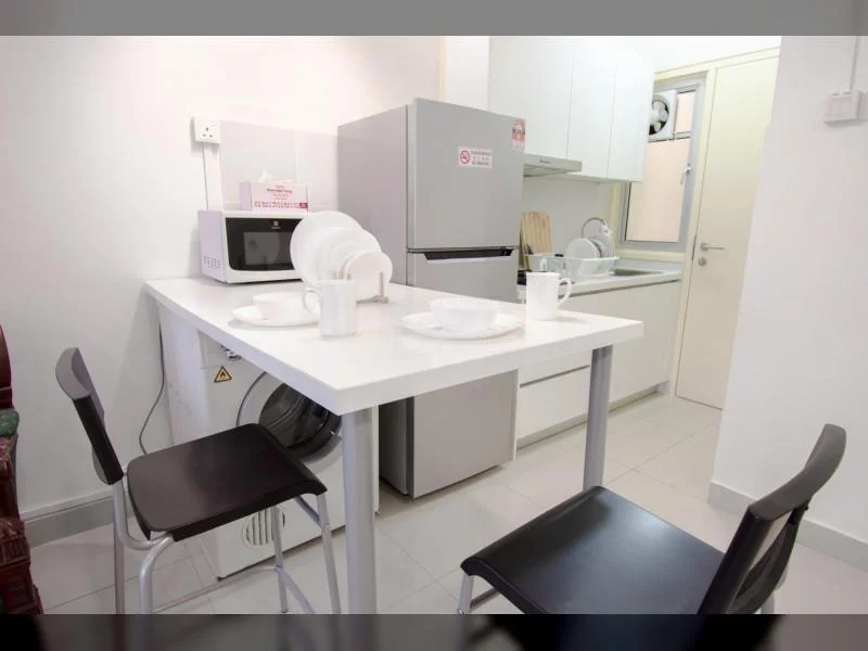Kitchen features: white cabinetry, stainless-steel fridge, microwave, white countertop, washing machine, ceramic tile flooring, white walls, single-bowl stainless-steel sink, chrome pull-down faucet, dining table for two, black plastic dining chairs; style: modern.