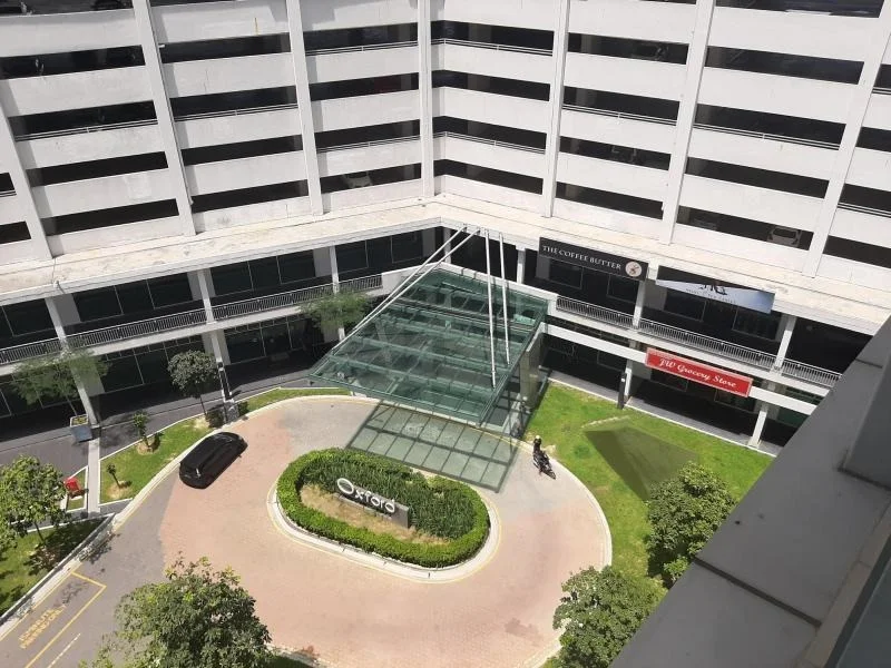 Exterior type: multi-storey car park; features: glass entrance structure, landscaped garden area, manicured lawn, trees planted around the entrance, paved walkway, signage for Oxley, open-air parking spaces, surrounding greenery; style: modern.