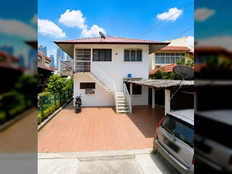Exterior type: semi-detached house; features: double-storey, white painted facade, red tiled pitched roof, projecting roof eaves, external staircase to upper floor, covered car porch with awning, driveway with terracotta tiles, satellite dishes visible, barred windows, fronts a quiet residential street, surrounded by mature greenery; style: traditional.