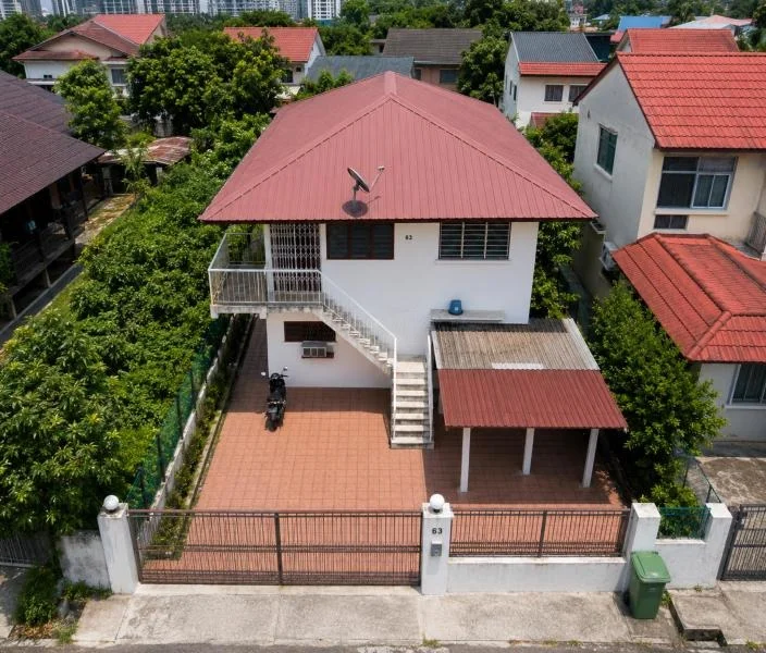 Exterior type: detached bungalow; features: double-storey, white painted facade, red pitched tile roof, projecting balcony, external staircase, covered car porch with corrugated metal roof, tiled driveway and front yard, metal front gate, perimeter fence, surrounded by mature greenery, fronts a quiet residential street; style: traditional.