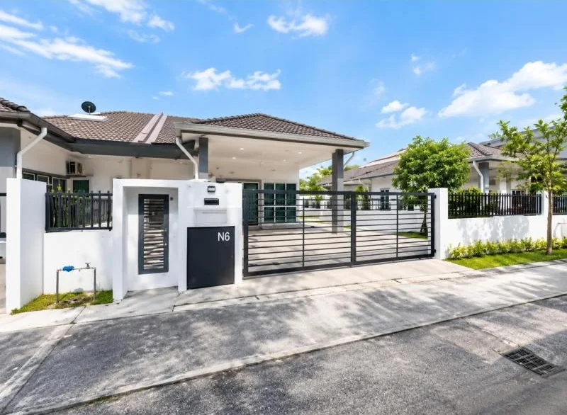 Exterior type: detached bungalow; features: single-storey, white painted facade, grey trim accents, pitched tile roof, covered car porch, double gate, black metal fence, white perimeter wall, fronts a quiet residential street, small landscaped lawn, young trees, driveway with concrete paving, gated entry, mailbox at entrance; style: contemporary.