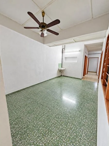 Room features: white painted walls, green terrazzo flooring, flat white ceiling, exposed ceiling beams, 5-blade ceiling fan with light, fluorescent tube light, small wall-mounted sink, built-in wall niche, wooden louvered window shutters, wooden door frames, narrow hallway opening, built-in wooden shelving, recessed ceiling section; style: traditional.