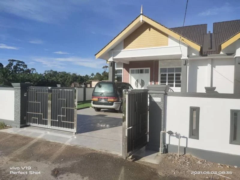 Exterior type: detached bungalow; features: grey painted facade, gabled roof with brown tiles, manicured lawn, paved driveway, metal gate, front porch, single-storey, surrounded by greenery; style: modern.
