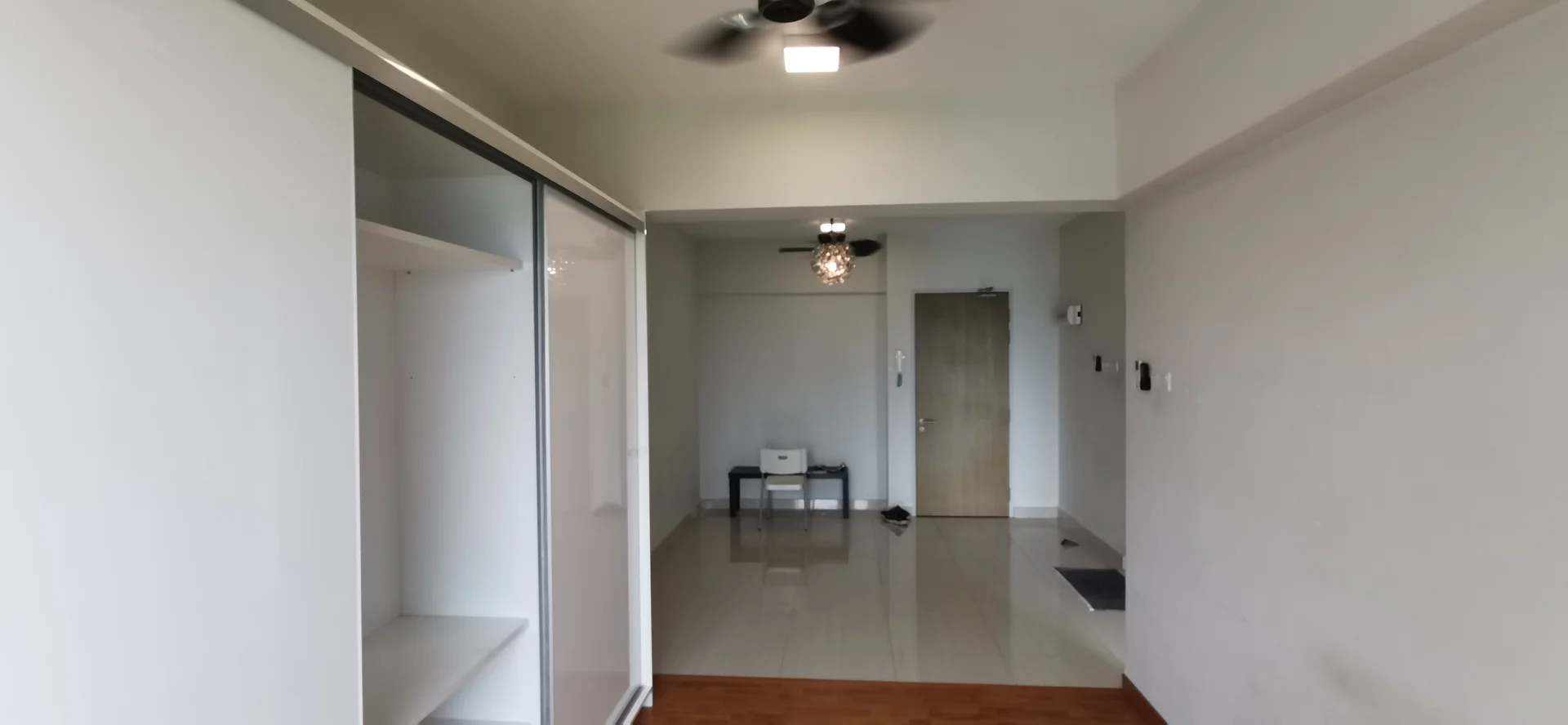 Room features: white painted walls, glossy tile flooring, 5-blade ceiling fan with light, sliding wardrobe with mirror, wooden flooring at entrance, door with security lock, light fixture, neutral decor; style: modern.