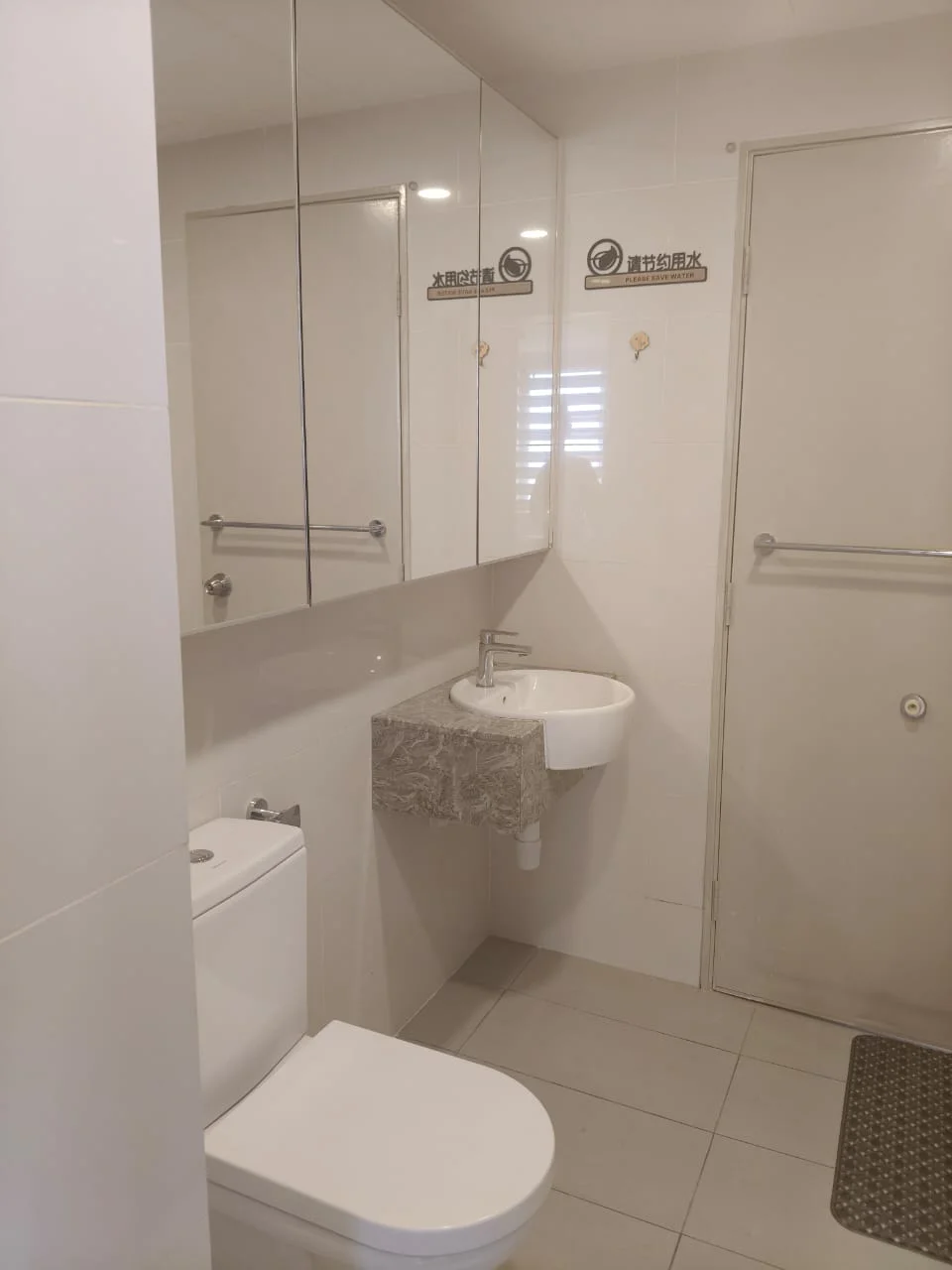 Bathroom features: white tiled walls, grey tiled flooring, single-sink vanity with stone countertop, chrome basin mixer faucet, one-piece toilet, framed mirror above sink, wall-mounted towel rack, shower area with glass partition; style: modern.