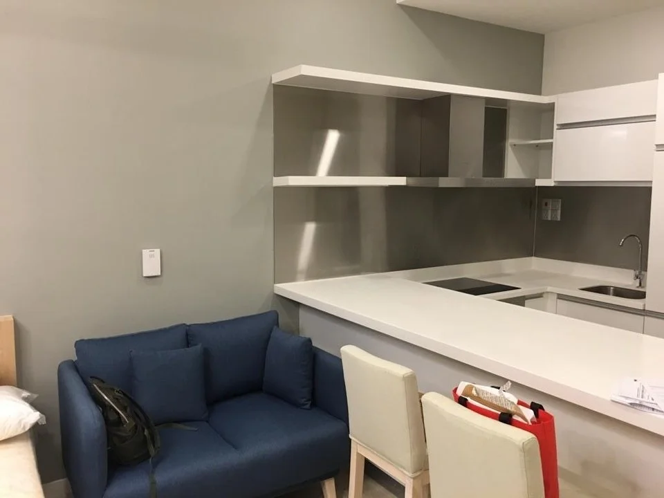 Kitchen features: stainless-steel countertop, white cabinetry, open shelving, built-in oven, 4-burner induction hob, single-bowl stainless-steel sink, chrome pull-down faucet, grey painted walls, recessed downlights; style: modern. Living features: blue fabric sofa, wooden legs on sofa, white dining chairs, neutral colour palette, minimalist decor; style: modern.