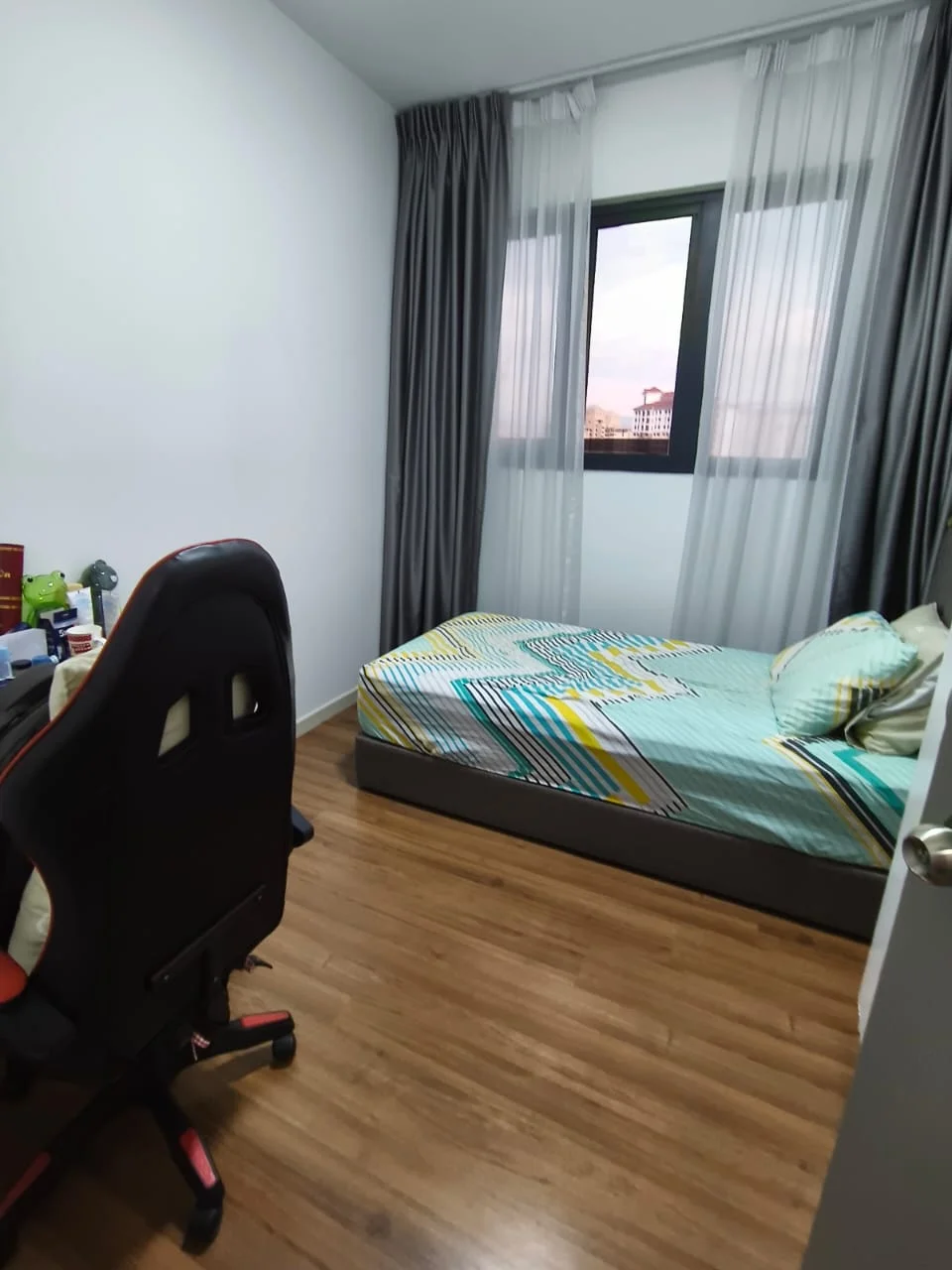 Bedroom features: queen-size bed with patterned bedding, wooden flooring, white painted walls, floor-to-ceiling window with sheer curtains, desk with office chair, decorative pillows, nightstand, wall-mounted light fixture; style: modern; view: city.