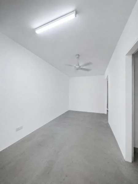 Room features: white painted walls, grey concrete flooring, sloped ceiling, fluorescent tube ceiling light, 3-blade ceiling fan, plain white ceiling, doorway opening on right side, empty unfurnished room, rectangular room layout, smooth painted wall finish; style: minimalist.