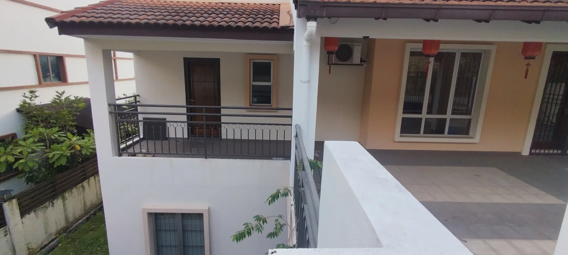 Exterior type: linked terrace house; features: terracotta tile roof, white painted facade, balcony with metal railing, ground floor patio, visible air conditioning unit, landscaped garden area, sliding glass door, window with grille, lanterns hanging from eaves; style: modern.