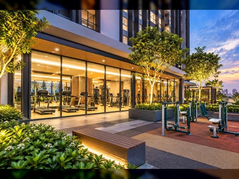 Exterior type: clubhouse; features: glass curtain wall, modern high-rise podium facade, approximately 20-storey high-rise, recessed balconies, flat roof, landscaped podium deck, manicured shrubs, mature trees, outdoor gym, exercise machines, seating bench, illuminated walkway, city skyline in background, tropical landscaping; style: modern.