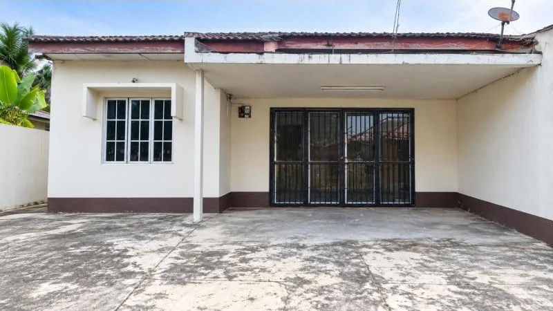 Exterior type: detached bungalow; features: single-storey, white painted facade, brown base trim, pitched tile roof, covered car porch, double-width car porch, concrete driveway, front security grille gate, sliding glass door behind grille, single window with white frame, surrounded by mature greenery; style: traditional.