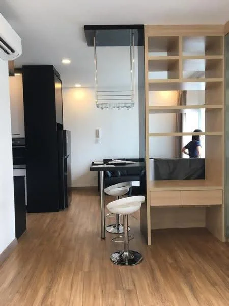 Room features: wood laminate flooring, white painted walls, black cabinetry, stainless-steel fridge, built-in shelving unit, glass dining table, white bar stools, recessed ceiling lights, air conditioning unit; style: modern.