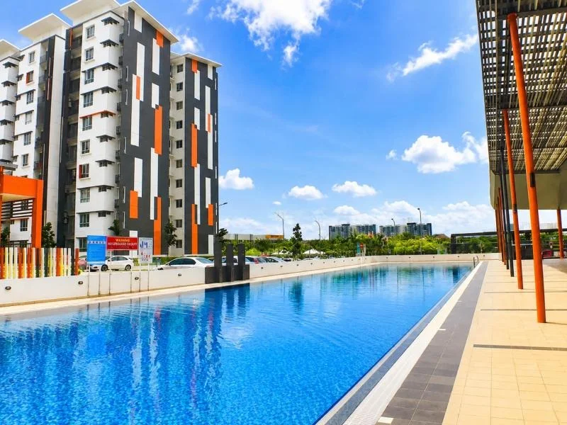 Exterior type: swimming pool deck; features: infinity pool, pool deck with loungers, covered walkway, perimeter fence, open-air parking lot, high-rise residential towers, approximately 10-storey high-rise, white painted facade, dark grey facade panels, orange vertical accent panels, projecting balconies, flat roof, tropical landscaping, skyline view in background; style: modern.