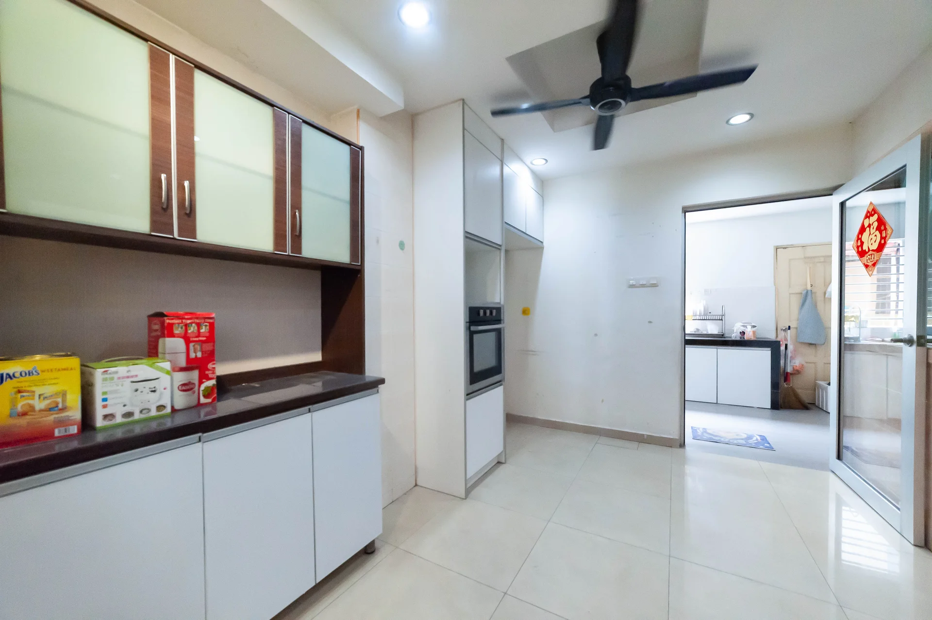 Kitchen features: white cabinetry with glass panels, dark countertop, built-in oven, stainless-steel range hood, ceramic tile flooring, recessed downlights, 5-blade ceiling fan, open layout to adjacent room, kitchen appliances including microwave and rice cooker, wall-mounted cabinets; style: modern.