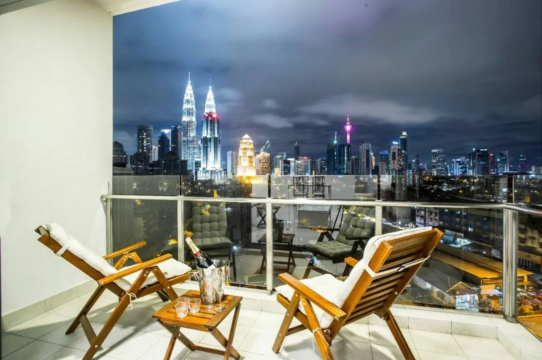 Balcony features: glass railing, outdoor seating with wooden chairs, small side table, city skyline view, night lighting, tiles flooring; style: modern; view: city.
