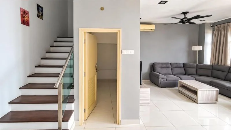 Living features: white painted walls, large-format white tile flooring, grey accent wall, sectional L-shape sofa in grey fabric, rectangular coffee table with wood finish, wall-mounted air conditioner, black ceiling fan, recessed ceiling lights, floor-length beige curtains, glass balustrade staircase, dark wood stair treads, metal handrail, small wall art pieces, open doorway to adjacent room, white ceiling, minimalist decor; style: modern. Hallway features: white painted walls, large-format white tile flooring, open doorway, light yellow door, adjacent utility or storage room visible; style: modern.