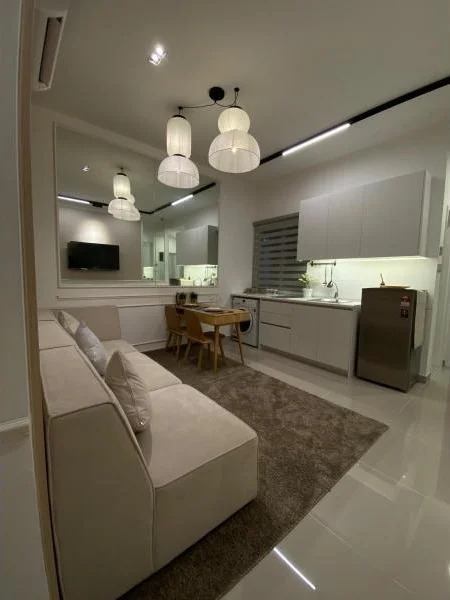 Living features: 3-seater fabric sofa in cream, area rug with neutral color, dining table for 4, white cabinetry, stainless-steel fridge, built-in oven, ceramic tile flooring, recessed downlights, pendant lights, wall-mounted TV, window with blinds, mirror on wall; style: modern.