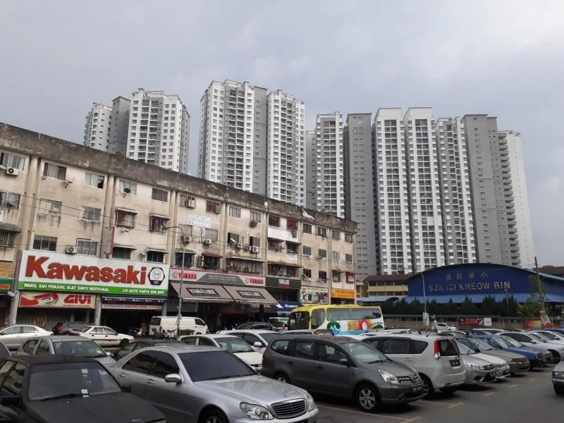 Exterior type: high-rise condominium; features: multiple high-rise buildings, commercial shops at ground level, parking lot with multiple vehicles, signage for various businesses, urban setting with cloudy sky; style: modern.