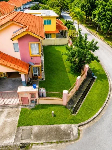 Exterior type: semi-detached house; features: double-storey, pink painted facade, yellow painted facade, cream painted facade, red clay tile roof, projecting balconies, front yard lawn, stone-paved driveway, gated entry, perimeter fence, corner lot, fronts a quiet residential street, surrounded by mature greenery, drainage ditch along roadside; style: contemporary.