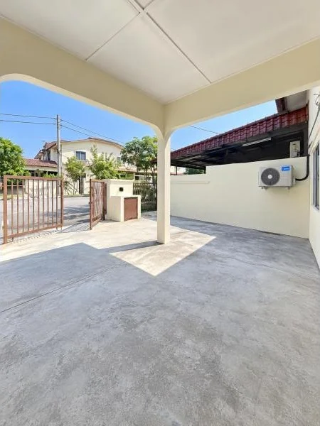 Exterior type: linked terrace house; features: covered car porch, single-storey, cream painted exterior walls, flat roof canopy, concrete flooring, metal swing gate, boundary wall, fronts a quiet residential street, air-conditioning condenser unit visible, neighboring terrace houses visible, tropical landscaping, mature trees; style: contemporary.