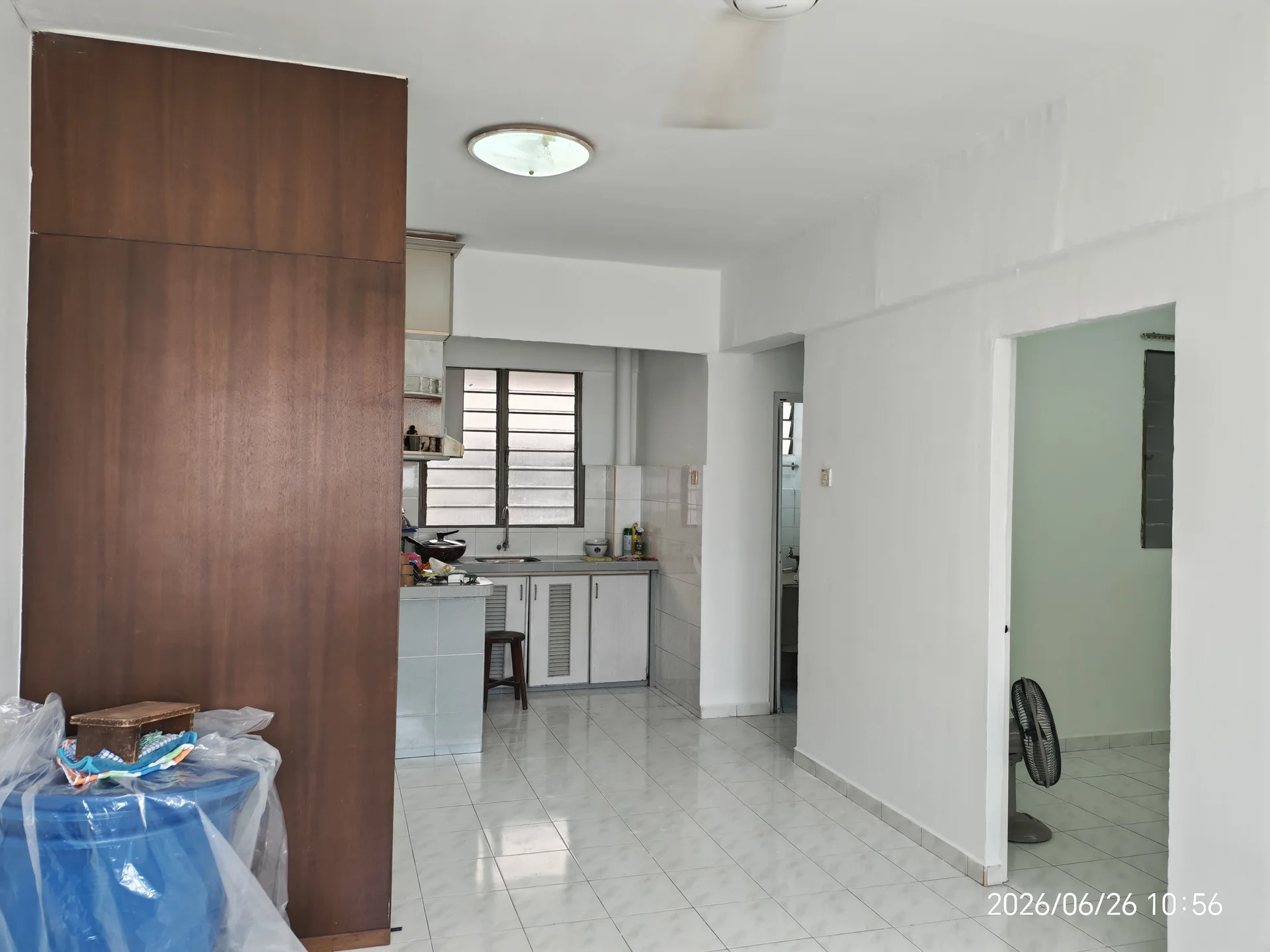 Kitchen features: white painted walls, glossy white tile flooring, ceiling light fixture, wood cabinetry, stainless-steel sink, countertop with backsplash, window with grid pattern, kitchen appliances visible, open layout to living area; style: modern. Living features: white painted walls, glossy white tile flooring, ceiling light fixture, open layout to kitchen, fan, doorway to hallway; style: modern. Room features: white painted walls, glossy white tile flooring, doorway leading to another room.