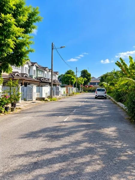 Exterior type: townhouse; features: double-storey, white painted facade, pitched tile roof, recessed balconies, fronts a quiet residential street, front boundary walls and gates, covered car porch with awning, open-air parking along street, stone-paved roadside verge, mature trees, tropical landscaping, utility poles and overhead cables; style: contemporary.
