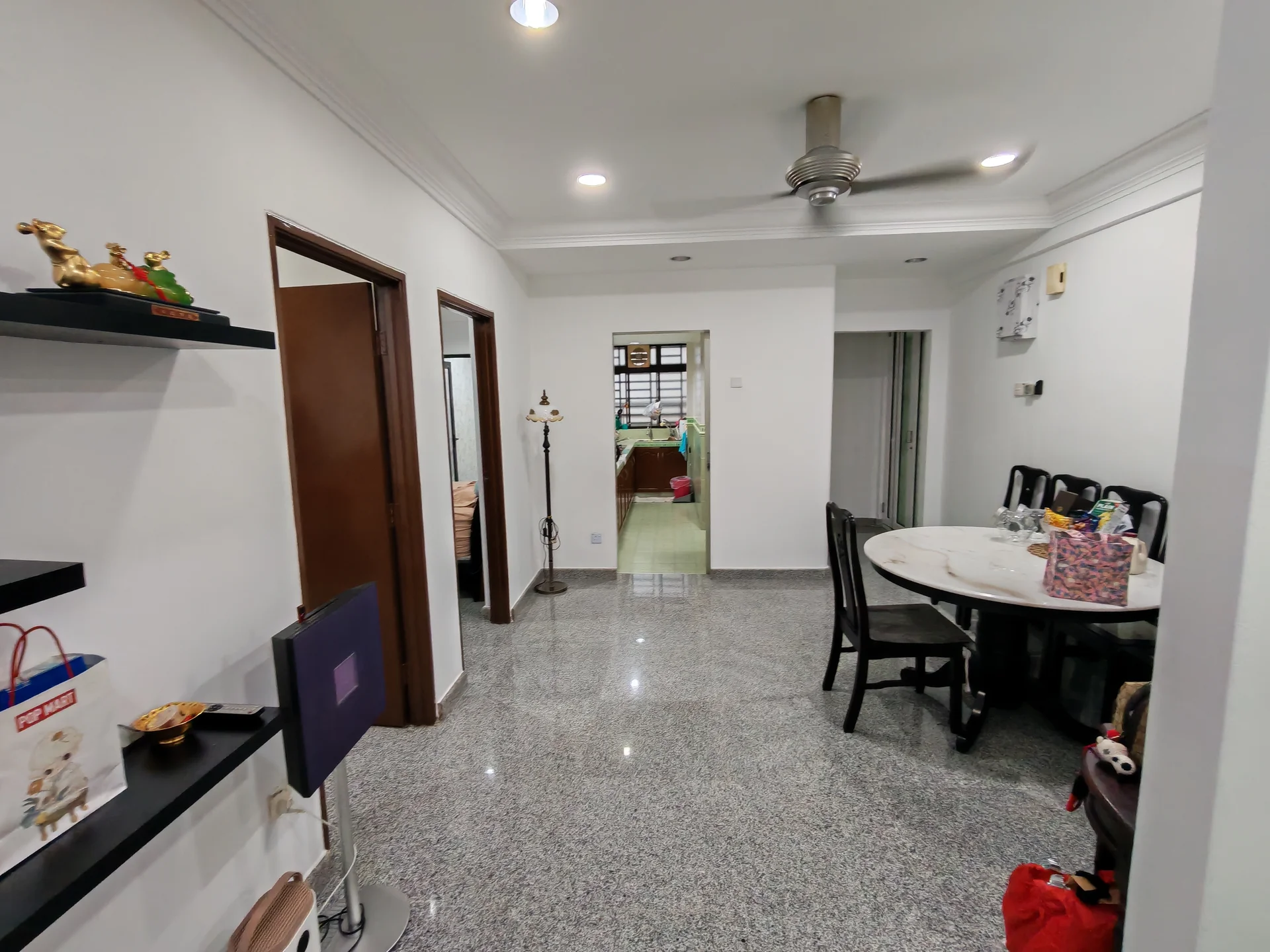 Room features: white painted walls, grey granite flooring, 5-blade ceiling fan, recessed downlights, round dining table, black dining chairs, decorative items on shelf, doorway leading to kitchen, doorway leading to bedroom, wall-mounted TV, floor lamp; style: modern.