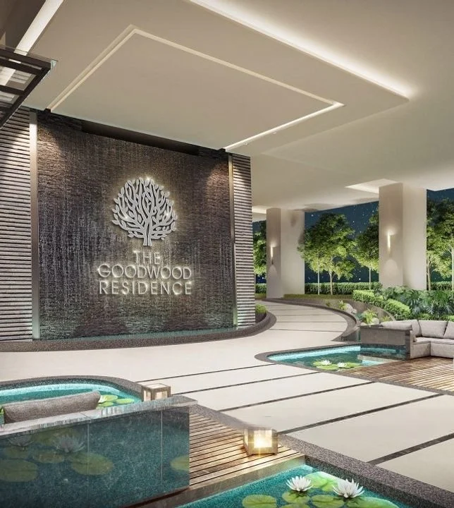 Exterior type: clubhouse; features: water feature with lotus flowers, decorative stone wall with logo, landscaped garden with greenery, pathway with stone paving, outdoor seating area with sofas, ambient lighting, modern architectural design, nighttime illumination; style: modern.
