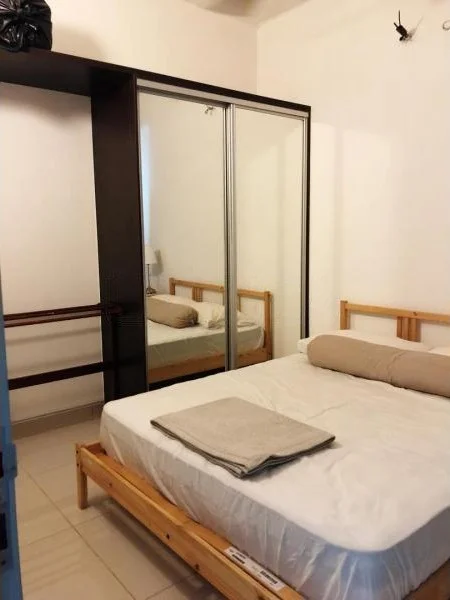 Bedroom features: queen-size bed, wooden bed frame, mirrored sliding wardrobe, bedside lamp, white bedding, rolled towel on bed, light-colored tiled flooring, wall-mounted light fixture; style: minimalist.